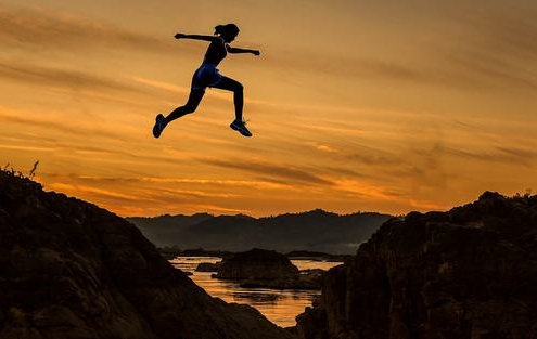 Eine sportliche junge Frau springt über einen Graben in goldener Abendsonne